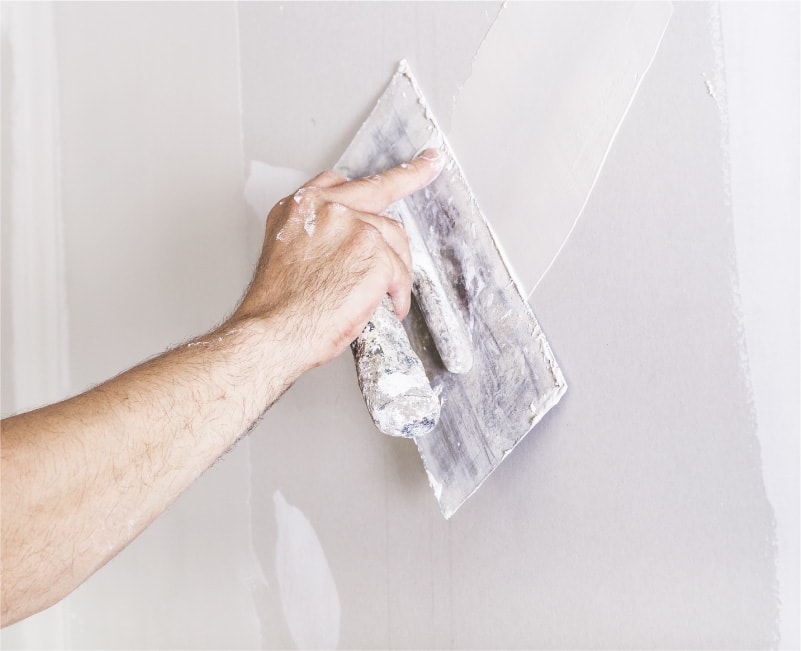 A painter repairs a wall with putty to prepare an interior wall for painting