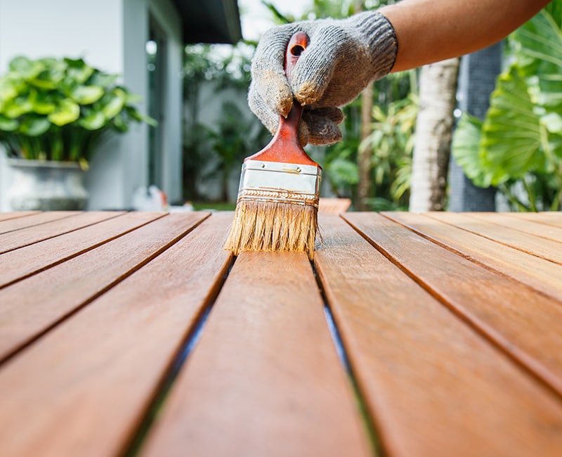 A painter brushes on a fresh coat of wood stain to refresh a backyard deck